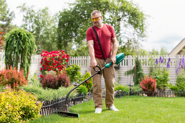 Middle aged man trimming grass with weed cutter, taking care for his backyard. The concept of a beautiful garden