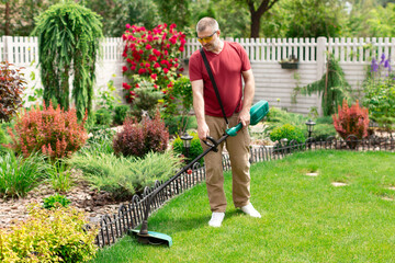 Middle aged man houseowner cutting grass with weed cutter on his grassy lawn. Seasonal gardening...