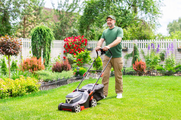 Middle aged man houseowner mowing the lawn on backyard of his house, making beautiful landscape...