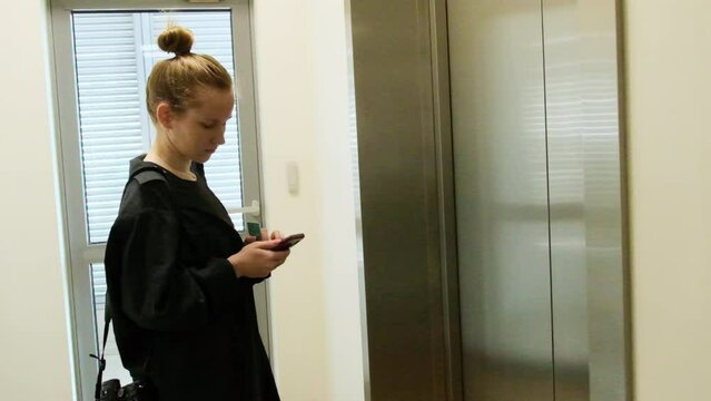 Blonde woman discusses important working issues in chat on mobile phone standing near elevator door. Lady near lift in office building