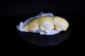 Ripe durian on black plate with black background. Durian fruit is in the middle with space for text. Eating sweet, ripe fruit, plants, organic product, and tropical fruit. Still-life durian texture.