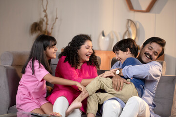 Father Mother And Kids Sitting On Sofa At Home Laughing While Spending  Time Together