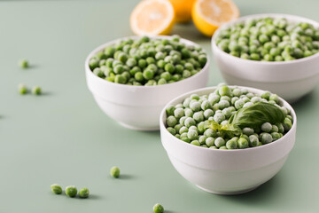 Three white bowls filled with frozen green peas on green background.