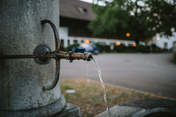 Old stone and iron faucet decorative public water fountain in Europe. Close up shot, flowing clean water, shallow depth of field, no people