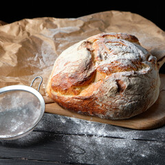 fresh loaf of bread sprinkled with flour on a wooden background