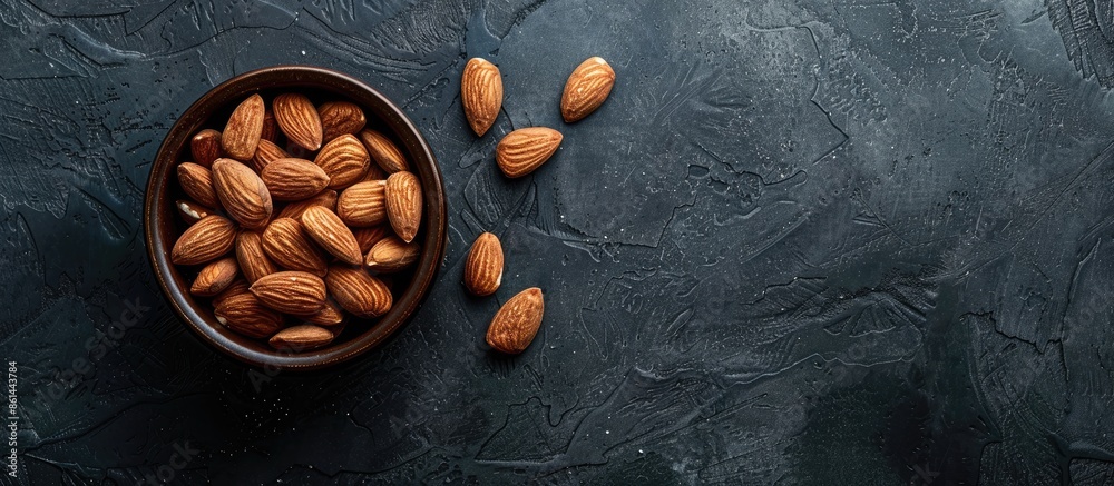 Poster almonds in a dark wooden bowl on a slate table for healthy diet concept with available copy space im