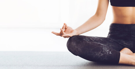 Cropped of woman is sitting cross-legged on a yoga mat in a lotus position, demonstrating flexibility and focus. She appears relaxed and concentrated, with hands resting on her knees, copy space