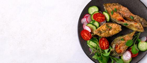 Oven baked pink salmon steaks with vegetable salad on dark plate on white table. Healthy meal. Mockup with copy space