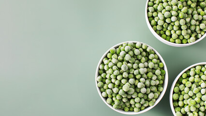 Three white bowls filled with frozen green peas on green background. Copy space