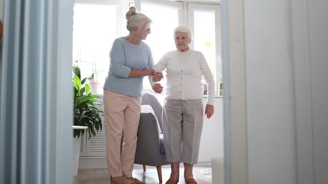 Caregiver helping elderly woman get up from the armchair
