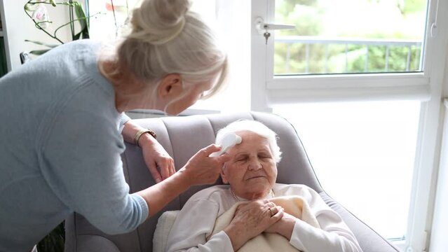 Caregiver using a body temperature monitor with elderly woman at her home