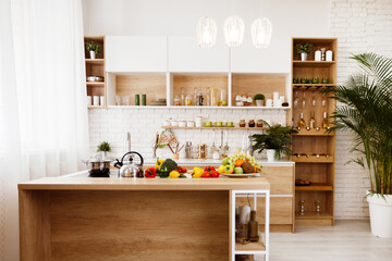 A modern kitchen island with fresh produce on display. The island is made of wood and has a white metal frame. There are several pieces of fruit and vegetables on the counter, including apples