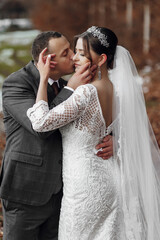 A bride and groom are kissing each other's lips. The bride is wearing a white dress and the groom is wearing a suit