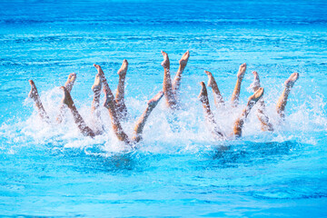 Artistic swimmers team performing synchronized legs choreographed movement in the swimming pool