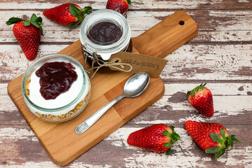 Glass jar full of muesli and yogurt with homemade strawberries jam, delicious snack with cheesecake and strawberries jam on wooden cutting board, detail with vintage cardboard tag
