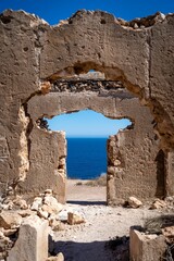 View of the ocean through the ruins of an old stone building on a sunny day.