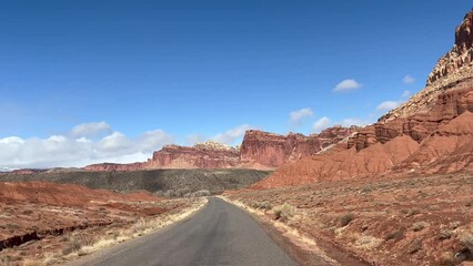 Point of view POV driving shot of the scenic drive in Capitol Reef National Park, Utah on a sunny day. Red rock formations and cliffs tower over the road, with stunning views of the desert - USA