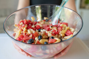 Bowl with fresh mixed fruit salad holding by woman´s hands. Homemade food