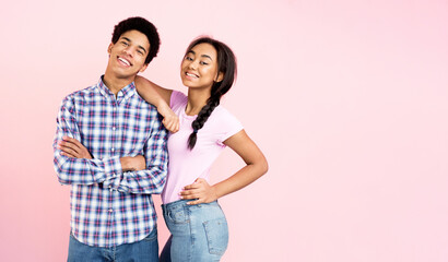 Naklejka premium Teen couple posing over pink background, girl holding hand on guy's shoulder