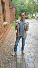 A man stands near an old brick wall and holds a thumbs up ok