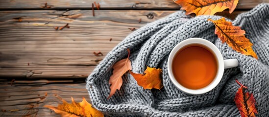 A scarf, tea or coffee, and autumn leaves set on a wooden background, with room for additional imagery.