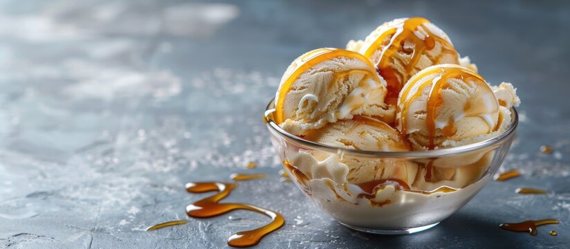 A glass bowl filled with tempting ice cream drizzled with caramel syrup on a neutral grey backdrop with ample copy space image.