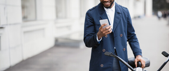 An African American businessman is commuting to his office by bicycle, using his phone. The mood is...