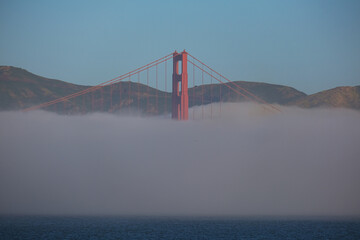 World famous red steel suspension bridge in San Francisco port entrance with Golden Gate State park nature lands hidden in cloud mist fog bank with clear sky pilars