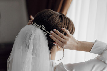 A woman is getting ready for a wedding and is putting on a veil. The veil is made of lace and has a...