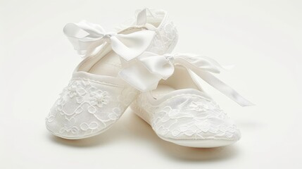 A pair of white knitted baby booties with a satin bow sits next to a white knitted blanket on a white background