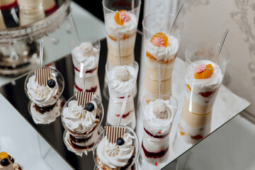 A table with a variety of desserts in clear plastic cups. The desserts include a blueberry cake, a strawberry shortcake, and a vanilla pudding. The table is set up for a party or gathering
