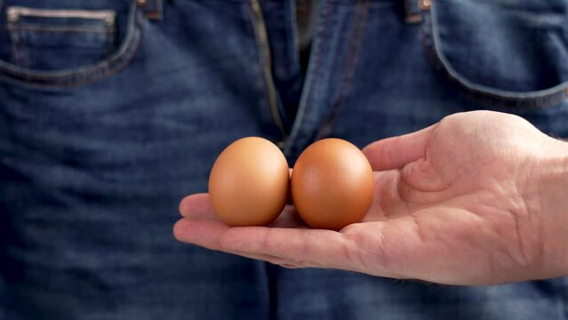 Two eggs in male hand on man jeans background. Infertility and urological diseases concept