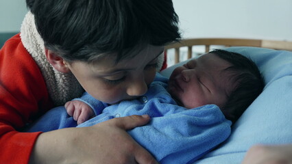 Tender moment between a young boy and his newborn sibling, captured as the boy kisses the baby, dressed in blue, showcasing love, family bond, and the arrival of a new family member