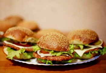 Homemade delicious burgers with lettuce, cheese, tomato, onion.  Cheese burger plate on wooden table. Tasty grilled & appetizing burger or cheeseburger. Lot of hand made classic recipe sandwich bun