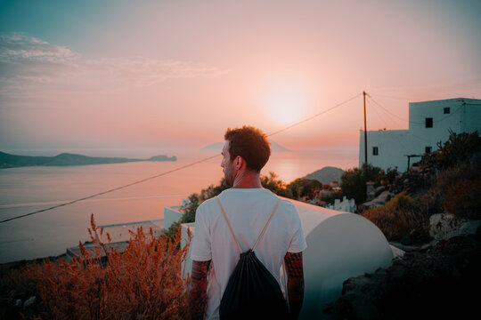 Young tattoed man standing against a summer sunset on an island, blurry background
