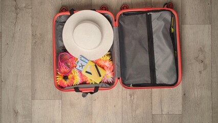 A peach-colored suitcase with summer clothing and travel essentials of top view