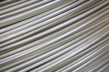 Close-up of coiled aluminum wires, highlighting their smooth surface and layered overlapping pattern, captured in soft lighting..