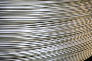 Close-up of coiled aluminum wires, highlighting their smooth surface and layered overlapping pattern, captured in soft lighting..