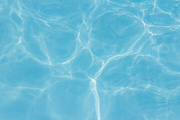 Clear blue swimming pool water surface with sunlight reflections creating abstract patterns and ripples, evoking a refreshing and tranquil summer vibe.