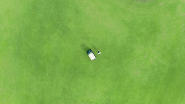 Golf Cart buggy on green in overhead aerial drone view. Sunny day on a tropical green playground. Aerial footage of people on a golf course playing the sport in Hawaii