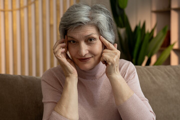 An elderly woman is sitting on the couch in the living room. She's wearing a pink turtleneck...