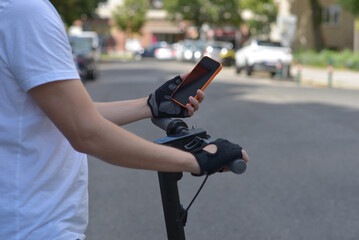 A man on an electric scooter using smartphone. Close up photo of hands in sport gloves. The concept of ecology and healthy lifestyle in the city