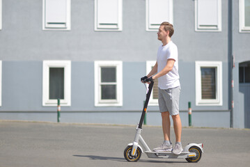 A man in casual sport wear rides electric scooter at the background of a building. Side view. The concept of ecology and healthy lifestyle in the city © Anastasiia