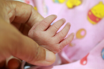 Mom and newborn baby girl holding hands on pink blanket background.