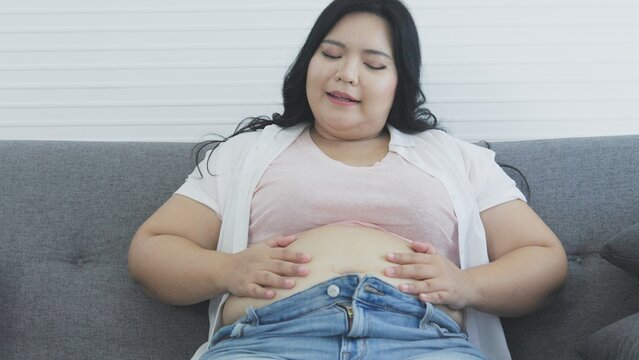 chubby asian woman smacks her belly happily after eating food the pleasure of eating fat woman