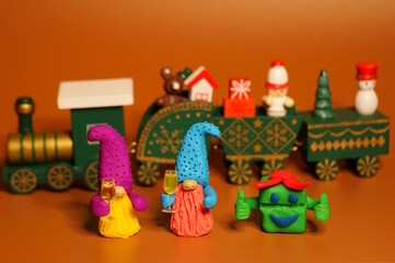 Two toy dwarfs made of plasticine with glasses of champagne on the background of a Christmas train. New Year's holidays and Christmas. Decorations and decorations.