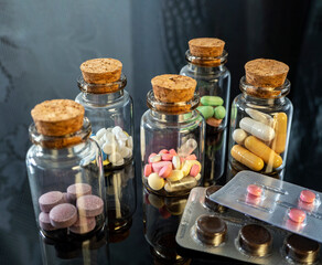 Tablets and capsules in glass bottles and blisters placed on a black reflective surface. Background with medicines for industry, business, pharmacies and clinics.