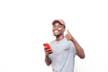 A young african man in a casual outfit gives a thumbs-up while holding a smartphone, expressing positivity and approval.