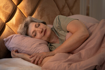 At night, an elderly woman can be seen sleeping soundly in bed. She is covered with a blanket, and...