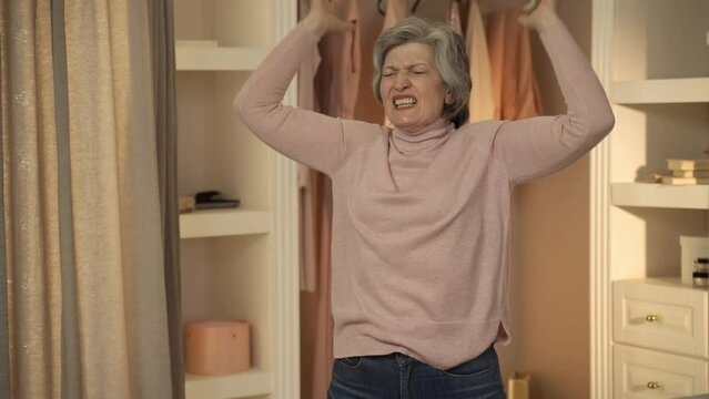 Elderly woman in a closet throwing clothes around while getting dressed. She appears to be frustrated and in a hurry